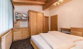 A cozy bedroom with a large bed, a wooden wardrobe, and a television. The walls are painted in soft colors, creating a pleasant atmosphere.