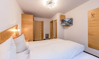 A modern bedroom with a double bed and a TV. The walls are painted light, and there are wooden furniture pieces that create a cozy atmosphere.