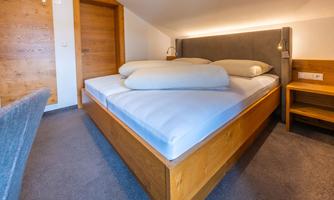 A cozy bedroom with a large double bed and comfortable pillows. The walls are painted in neutral tones and there is a warm lighting ambiance.