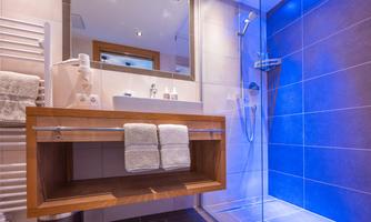 A modern bathroom with a shower cubicle and an elegant sink. Towels are laid out on a wooden shelf.