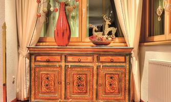 A stylish interior with a decorative wooden cabinet and a red vase. The windows feature bright curtains and a pleasant light glow.