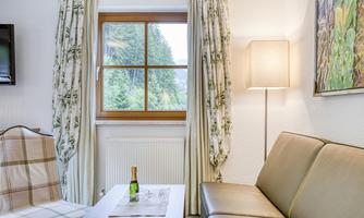 A cozy living space with a window overlooking a green landscape. On the table is a bottle of wine and a glass.