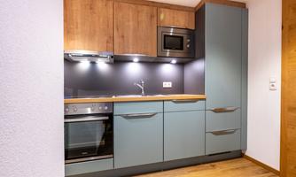 A modern kitchen with wood-colored upper cabinets and blue lower cabinets. It is equipped with an oven, a stove, and a microwave.