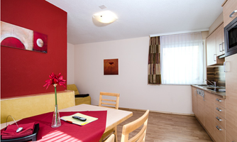 A friendly living area with a dining group and modern kitchen equipment. The walls are designed in warm colors, and a floral arrangement gives the room an inviting atmosphere.