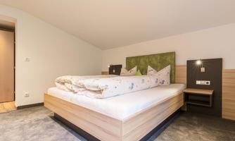 A modern bedroom with a large bed and cozy bedding. The walls are kept neutral and create a relaxing atmosphere.