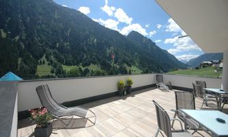 A sunny balcony with a view of the mountains. Relaxed loungers and tables provide a cozy outdoor spot.