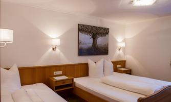 A cozy room with two beds and modern lamps. A painting of a tree hangs on the wall.