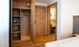 A modern hotel room with a wooden wardrobe and a door to a bathroom. The floor is made of wood and the atmosphere is bright and inviting.