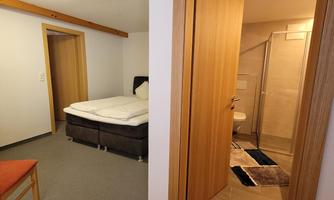 A cozy room with a double bed and a small table. In the background, there is a bathroom with a shower.
