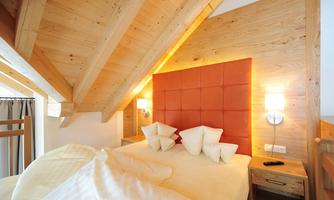 A cozy bedroom with wooden paneling and a large bed. The orange headboard and modern lamps create a warm atmosphere.