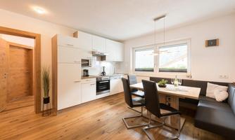 A modern kitchen with wooden flooring and a cozy dining area. The furnishings are bright and inviting.