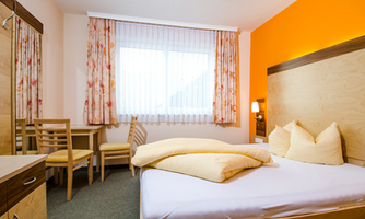 A cozy room with a double bed and yellow pillows. The walls are orange, and there is a small table with chairs.