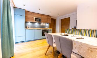 A modern kitchen with wood and blue cabinets. A table with gray chairs is in the foreground.