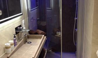 A modern bathroom with an elegant shower cabin and blue lighting. Next to the shower is a stylish sink with accessories.