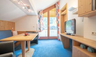 A cozy living area with wooden details and a large window. The room is bright and welcoming with a table and a television.
