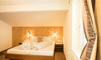 A cozy bedroom with a large bed and stylish wooden details. The room is bright and inviting, with a window view.