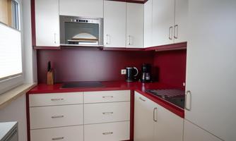 A modern kitchen with a red background and white furniture. There is a microwave, a kettle, and a coffee machine on the countertop.
