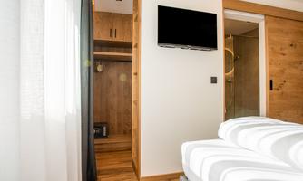 A modern hotel room with a television on the wall. On the left side is a wardrobe and on the right is the bathroom.