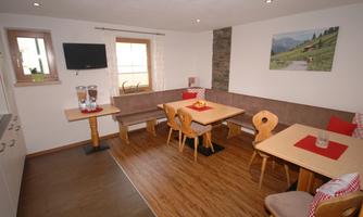A cozy room with wooden floors and modern design. There are tables, a seating area, and a small kitchen nook.