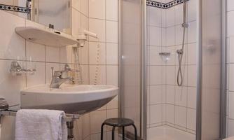 A small bathroom with a shower cubicle and a bright tiled floor. The walls are tiled and there is a sink with a mirror.