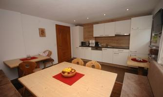 A modern kitchen with bright furniture and a large table. On the table sits a bowl of fruit.
