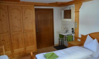 A cozy room with wooden decor and a single bed. The room includes a wardrobe and a washbasin.