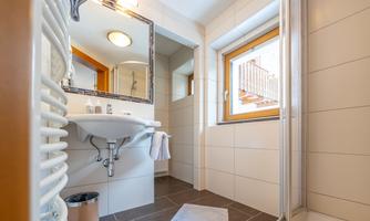 A modern bathroom with a sink, a mirror, and a shower. The window provides plenty of daylight.