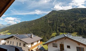 A picturesque mountain landscape with green forests and gentle hills. In the foreground, there are several cozy houses.