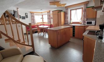 A modern kitchen with wooden cabinets and a seating area. The room has large windows and an open layout.