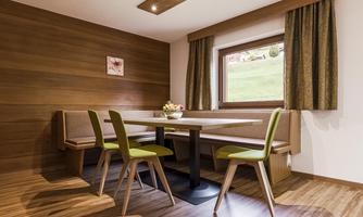 A cozy dining area with a table and modern green chairs. The walls are made of wood, and a window offers a view of the outdoor landscape.