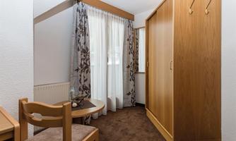 A cozy room with a table and chair, floral curtains, and a wooden cabinet. The room is bright and inviting.