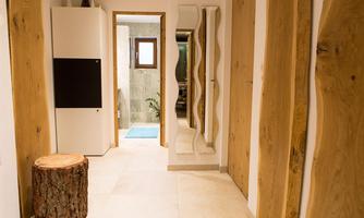 A modern hallway with bright walls and wooden details. On the left side, there is a refrigerator and a round wooden chair.