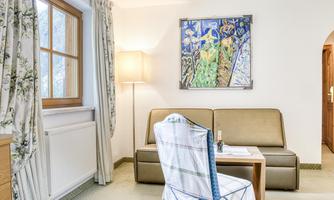 A cozy room with a couch, a table, and a lamp. A colorful picture hangs on the wall.