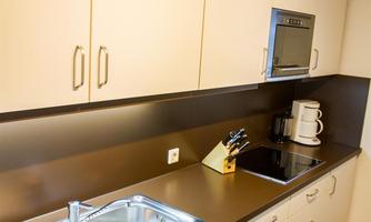 A modern kitchen unit with a sink, stove, and modern appliances. The cabinets are light-colored and the floor is made of wood.