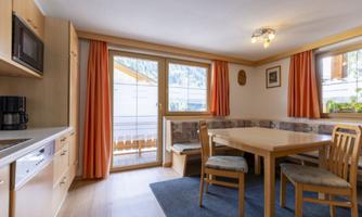A cozy kitchen with a dining table and chairs. Large windows ensure plenty of daylight and a view of the mountains.