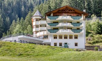 A modern hotel in the mountains with a traditional roof. Surrounded by green meadows and trees.