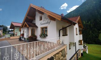 A charming house with a modern design, surrounded by nature. In the background, green mountains and a clear sky are visible.