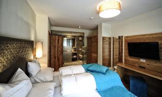 A modern hotel room with a large bed, soft pillows, and a TV. The decor is cozy and features wooden details and a bright bathroom.