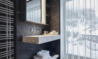A modern bathroom with an elegant vanity top and a large mirror. Through the window, a snow-covered landscape can be seen.