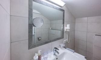 A modern bathroom with bright tiles and a large mirror. Various toiletries are on the sink.