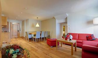 A modern living room with red furniture and hardwood flooring. The space is bright and inviting, featuring a dining table and an open kitchen.