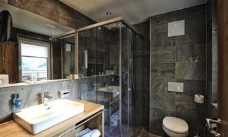 A modern bathroom with a glass shower and stylish tiles. The washing area features an elegant sink and wooden shelves.