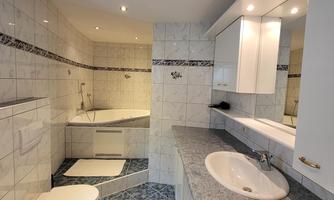 A modern bathroom with a bathtub and a bright shower. White tiled walls and an elegant sink create a clean atmosphere.