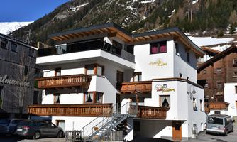 A modern building with several balconies in the Alps. Snow-covered mountains are visible in the background.