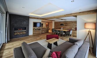 A modern living room with wooden floors and a cozy sofa corner. The room features a fireplace and a dining area.