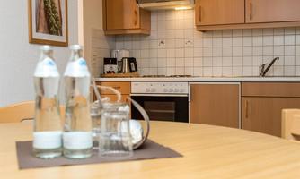 A modern kitchen with wooden cabinets and a stove. On the table, there are two bottles of water and a glass.