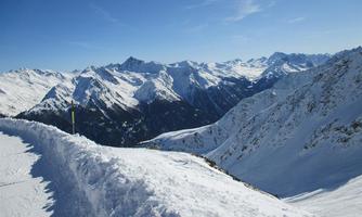 An impressive winter landscape with snow-covered mountains and a clear blue sky. The path is surrounded by snow and offers a magnificent view.
