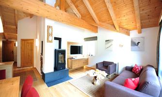 A cozy living room with wooden beam ceiling and modern furniture. The room is bright and inviting, with a television and a fireplace.