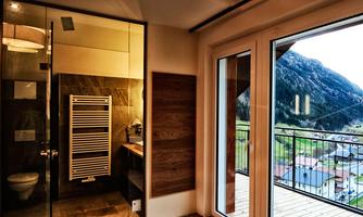 A modern bathroom with a glass shower and a towel radiator. Large windows provide a view of the mountains and the surrounding landscape.