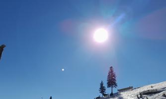A beautiful sunny day in the mountains with snow and a clear blue sky. A ski lift ascends the slope, surrounded by trees.